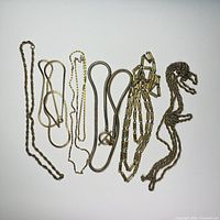 Six gold tone chains lying flat, displaying variety of styles and lengths, on a white background.
