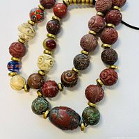 Close-up of carved large round beads in red, ivory, green, brown with gold separators on cord