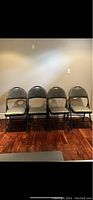 Four folding chairs lined up against a wall on a hardwood floor, showing full front view of seating and backrest.