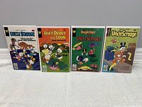 Four vintage Walt Disney comic books laid out side by side on white surface. Titles and cover characters visible.