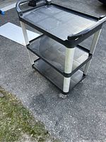 Side angled view showing three shelves with black plastic construction and metal legs.