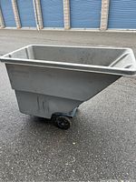 Side view of grey plastic dump truck container with wheel.