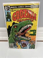 Godzilla comic book issue 16 with yellow cover showing Godzilla and man with gun, in protective bag and board.