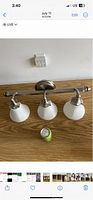 Photo of three-light bathroom fixture with frosted glass shades placed on wooden surface alongside a measuring tape for scale