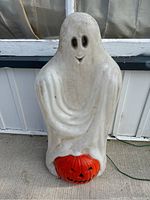 Front view of white ghost holding orange pumpkin blow mold decoration sitting on concrete.