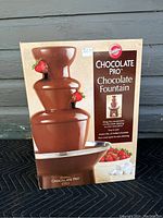 Box front showing the assembled Wilton Chocolate Pro Chocolate Fountain with strawberries and chocolate flowing down in three tiers.