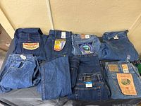Eight pairs of folded blue denim jeans in varying brands and sizes arranged on a surface to show variety in length, waist and label information.