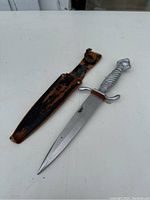 Full view of the metal blade with metal handle and worn leather sheath next to it