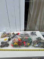 Full overview of all bags containing miniature action figures of various colors and sizes on a white table against a white wooden background.