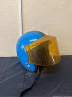 Side view of vintage blue motorcycle helmet with attached yellow visor, showing the helmet’s shiny surface and visor detail.