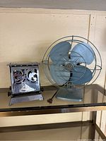 Full view of vintage blue-grey metal fan and chrome toaster side by side