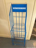 Full view of vintage blue metal newspaper stand with wire basket tiers for holding newspapers and prominent Toronto Star branding on top panel.