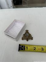 Image showing the pin next to a tape measure indicating approximately 2 inches wide, with a small box containing white padding.