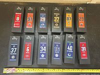 Photo shows 12 Tim Hortons collectible hockey sticks in individual black boxes with player jerseys and numbers visible, displayed on a black surface with measuring tape for scale