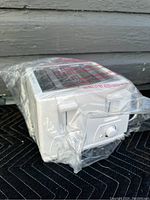 Side view of the white 4-slice toaster wrapped in plastic, showing side vents and plastic wrapping.