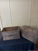 Two wooden CN shipping crates positioned on a black cloth surface against a wall, one open and one closed.