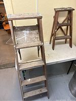 Front view of the two wooden step ladders, the taller on the left and the smaller on the right, showing paint wear and signs of use.
