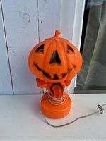 Front view of orange blow mold jack-o-lantern lamp showing facial details and coiled metal base element.