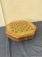 Angled view of the closed octagonal chess board showing floral and geometric patterns on top surface and sides.