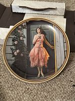 Front of Norman Rockwell limited edition decorative plate featuring a woman in a peach dress standing in a doorway with floral background and gold rim.