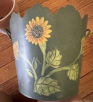 Green metal flower pot with sunflower painting and scalloped rim, showing exterior detail