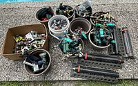 Wide view showing buckets and boxes filled with various garden hose attachments including sprinklers, valves, connectors, and nozzles on a patio floor near a pool.