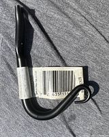 Photo of a single black garden hook with attached barcode label, displayed on a grey cloth surface.