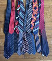 Photo showing 18 men's neckties arranged side by side on a wooden floor, highlighting varied patterns and red and navy blue colors.