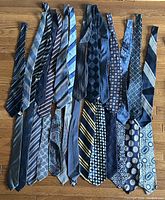 27 men's blue ties displayed flat on wooden floor, showing variety of patterns and colors.