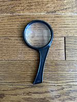 Small handheld magnifying glass with black handle on wooden floor
