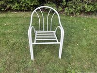 White curved back metal patio chair with arched back and rounded armrests on grass background.