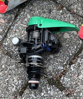Close-up of a single Rain Bird sprinkler head with a black body and green arm, showing details of springs and nozzle.
