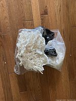 Photo showing large white sea coral pieces and black volcanic rocks placed on a wooden floor inside a plastic bag.
