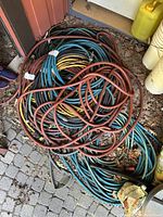 Coiled water hoses in red, blue, yellow, and brown colors piled on gravel outdoor surface.