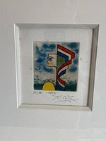 Full view of framed abstract art print showing the art centred with a white mat and frame. The artwork features abstract geometric shapes, hand-coloured in blue, red, yellow, and green, with visible numbering and signature below the image.
