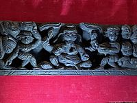 Front view of carved wooden panel showing three distinct ancient god figures in deep relief against red velvet backing.