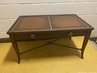 Front view of antique coffee table showing the leather topped surface with decorative gold tooling and two drawers with metal ring pull handles.