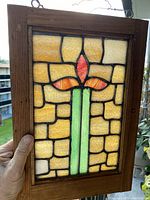 Photo of antique stained glass window featuring floral design in wooden frame held in hand to show scale.