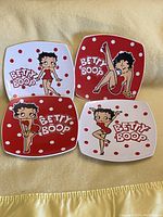 Four square Betty Boop porcelain dishes arranged on a yellow cloth, showing character poses and polka dot patterns.