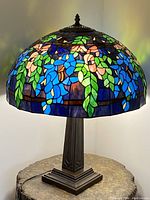 Full view of the illuminated stained glass lamp showing the colorful floral pattern and metal base.