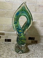 Front angled view of the vintage art glass sculpture showing green, blue and yellow swirls twisting upward from clear base with open center.