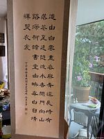 Photo of the full vintage Asian calligraphy scroll hung vertically, showing black ink characters and red stamps/signature on a cream fabric backing.