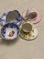 Photo showing four cups and four matching saucers arranged together on a white quilted surface, highlighting the varied floral designs and scalloped edges.