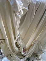 Close-up of cream cotton fabric with embroidered floral detail and ruched areas showing ties or gathers.