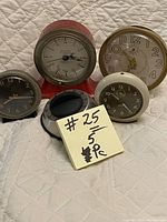 Front view of five vintage alarm clocks and timers arranged on a fabric surface with a pricing note in front.