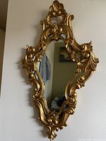 Full frontal view of the ornate gold leaf oval mirror hanging on a wall showing its detailed carved wood frame and mirror surface.