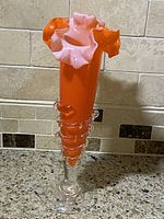 Front view of vintage orange art glass vase with ruffled pink edge and clear glass base placed on countertop.
