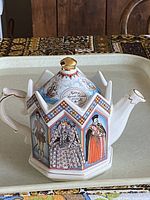 Hexagonal porcelain teapot featuring painted portraits of Queen Elizabeth I and historical figures, with gold accents on handle, spout, and lid knob.