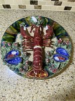 Top view of the entire ceramic plate showing the central lobster, oyster shells, and textured seaweed.