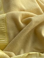 Close-up showing texture of yellow wool fabric and part of silk trim border.
